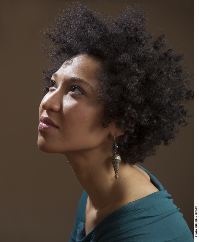 A profile view Julia Bullock of Julia Bullock wearing long earrings and a green dress.