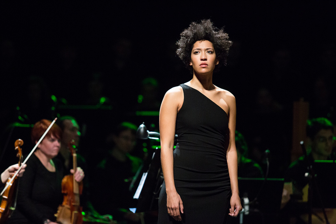 Julia stares seriously into the distance as she stands in front of an orchestra.