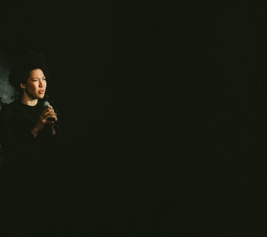 A dark image of Julia singing with a look of intensity.