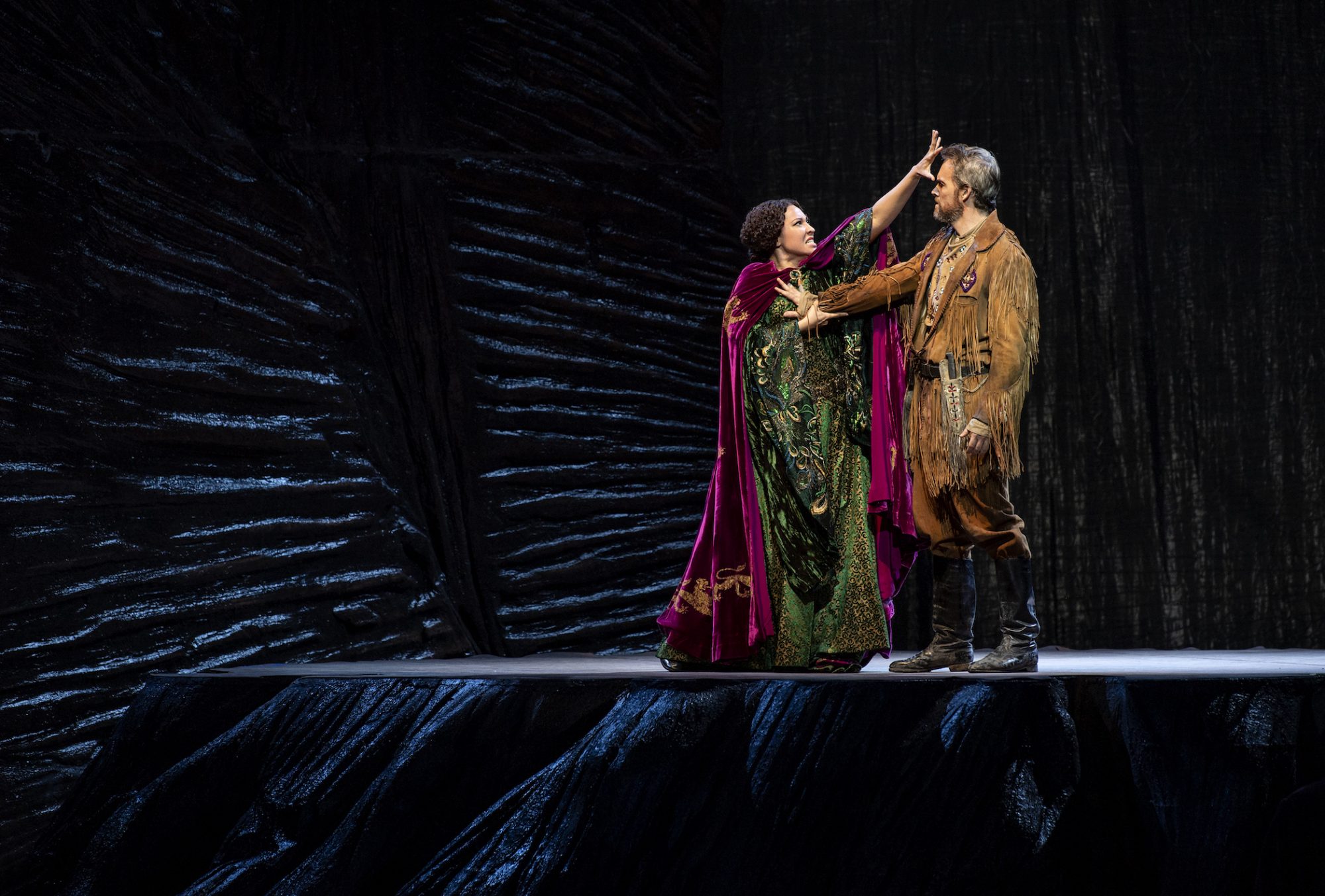 Julia Bullock performs in John Adams' 'Girls of the Golden West' for the Dutch National Opera. She wears a green gown and pushes against a man wearing a brown suit with fringes.