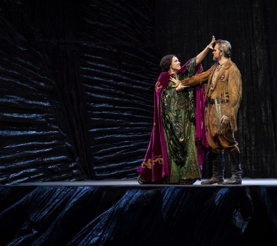 Julia Bullock performs in John Adams' 'Girls of the Golden West' for the Dutch National Opera. She wears a green gown and pushes against a man wearing a brown suit with fringes.