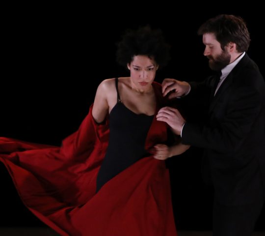 Julia Bullock stands beside a man who is removing a red jacket from her.