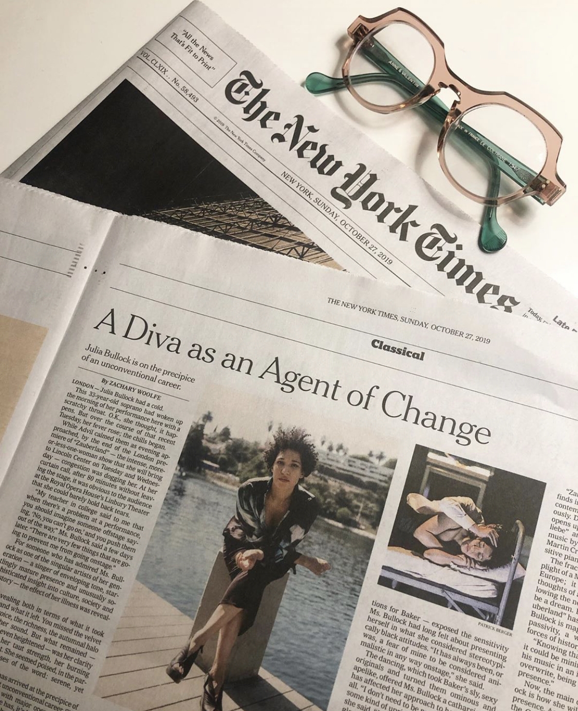 Julia Bullock's New York Times feature titled, "A Diva as an Agent of Change" on a table along with a pair of pink and green glasses.