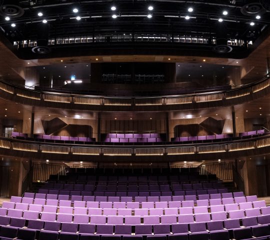 A panorama of Lindbury Theatre featuring purple seats and a view of the balconies.